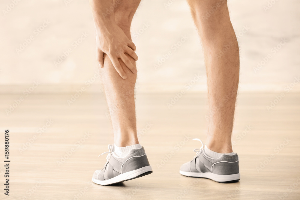 Young man suffering from pain in leg indoors