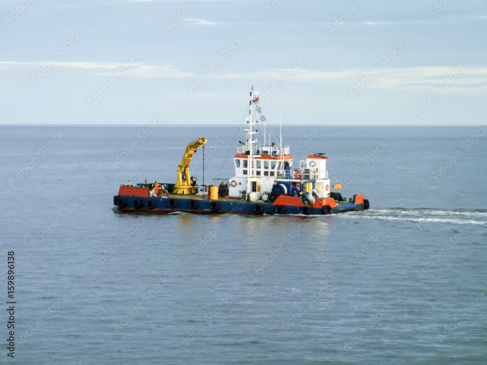A small service ship in a cargo industrial port. A ship in the sea A small service ship in a cargo industrial port. A ship in the sea