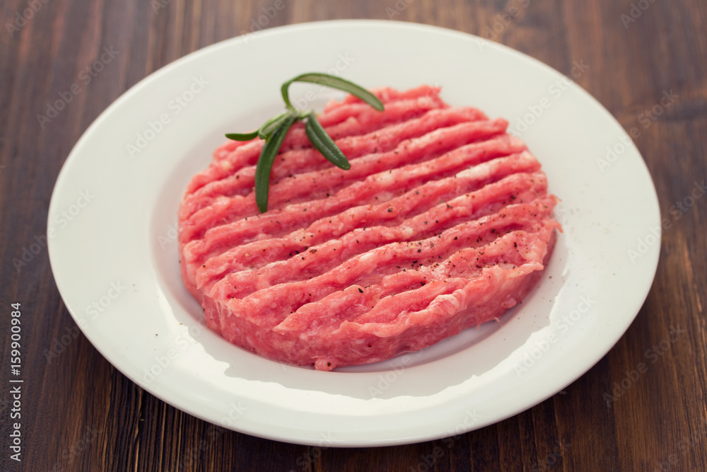 raw hamburger on white plate on wooden background raw hamburger on white plate on wooden background