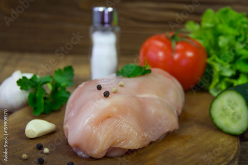 Raw chicken breasts on cutting board with parsley, garlic and peppercorn
