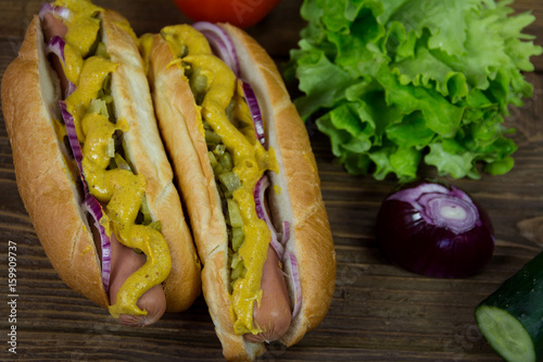 Hot dog with onion, mustard and pickles on wooden background