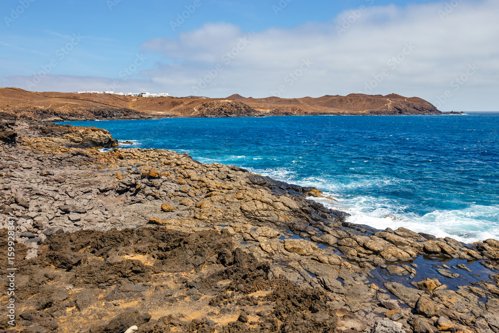 volcanic coastline with wavy ocean and blue sky, Lanzarote island, Spain