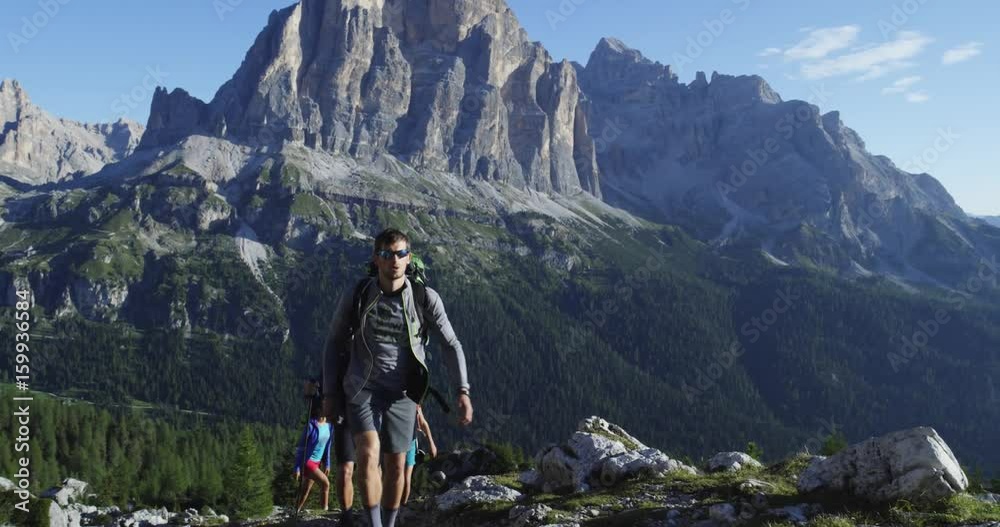 Four friends walking along hiking trail path. Group of friends people summer adventure journey in mountain nature outdoors. Travel exploring Alps, Dolomites, Italy. 4k slow motion 60p video