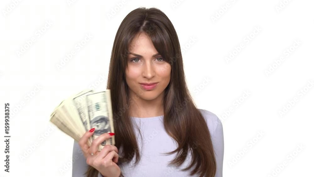 Concentrated young brunette female making hand fan from sheaf of dollars and waving it over white background Concentrated young brunette female making hand fan from sheaf of dollars and waving it over white background