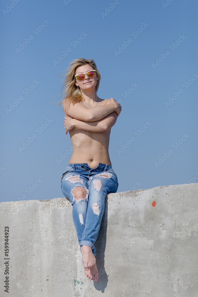 Topless young woman in torn jeans sits on concrete wall Stock Photo | Adobe  Stock