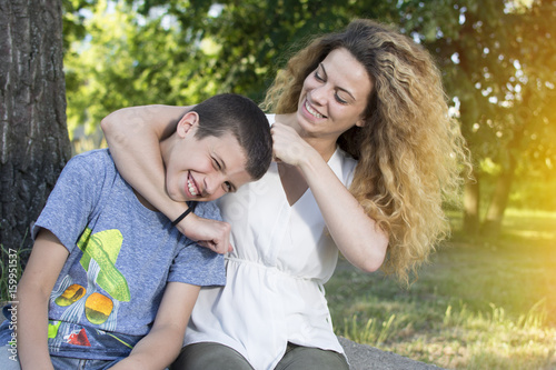 Siblings sitting together at the park. Big sister and little brother bonding. Smiling and having fun.