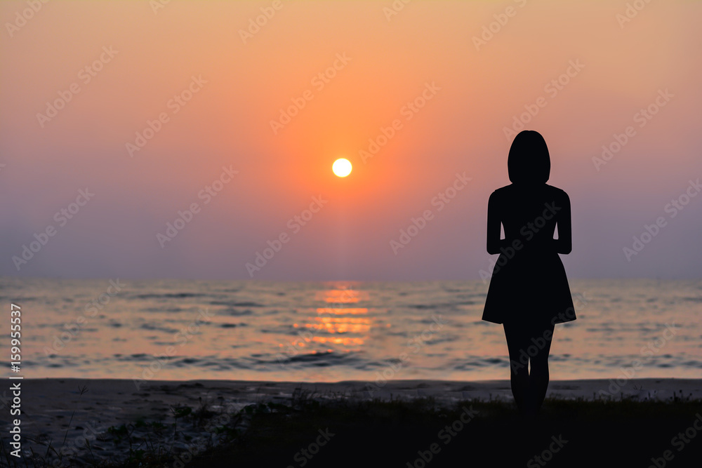 Silhouette of a woman standing by the sea and the sunset