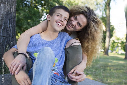 Siblings sitting together at the park. Big sister and little brother bonding. Smiling and looking at the camera.