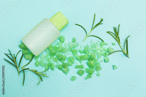 A bottle of essential oil and salt with fresh herb rosemary on a blue background.