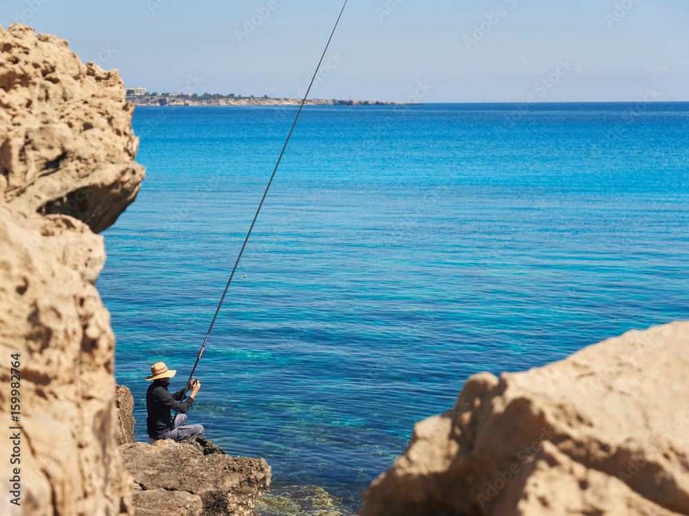 Man fishing in the sea from the rocky shore.