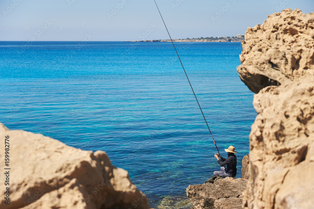 Man fishing in the sea from the rocky shore.