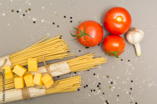 Ingredients for the preparation of pasta. Spaghetti, cheese, tomatoes, garlic, on a gray background. Top view.