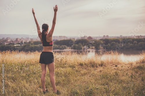 Sporty woman enjoys  exercising and looking at city view with her arms outstretched. © inesbazdar