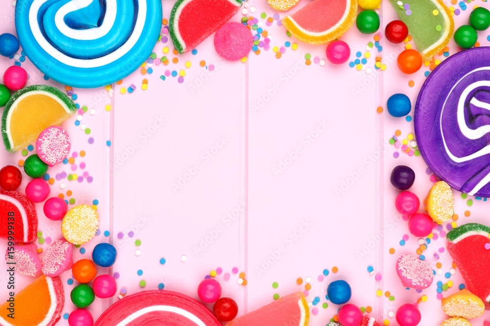 Frame of assorted colorful candies against a pink wood background