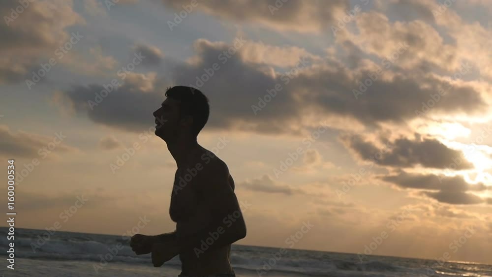 Young sporty man running on the sea beach at sunset. Athletic guy jogging along ocean shore during sunrise. Male sportsman exercising outdoor. Healthy active lifestyle. Workout at nature. Slow motion Young sporty man running on the sea beach at sunset. Athletic guy jogging along ocean shore during sunrise. Male sportsman exercising outdoor. Healthy active lifestyle. Workout at nature. Slow motion