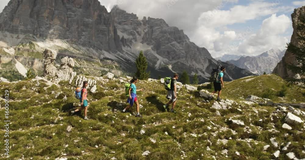 Four friends walking along wild hiking trail path. Group of friends people summer adventure journey in mountain nature outdoors. Travel exploring Alps, Dolomites, Italy. 4k slow motion 60p video