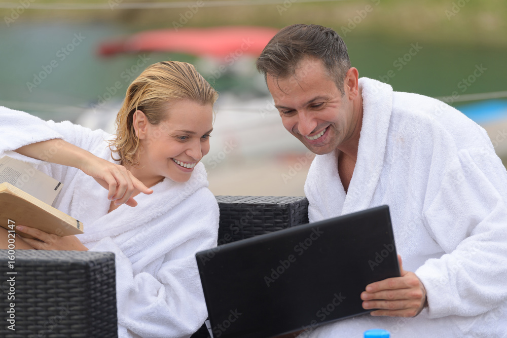 happy couple with computer at swimming pool lounge on terrace happy couple with computer at swimming pool lounge on terrace