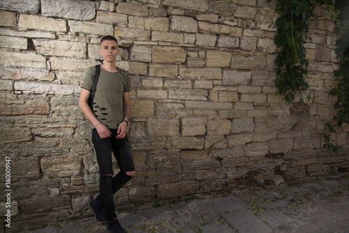handsome man in glasses standing against a stone wall wearing a black t-shorts looking straight in to camera. photo