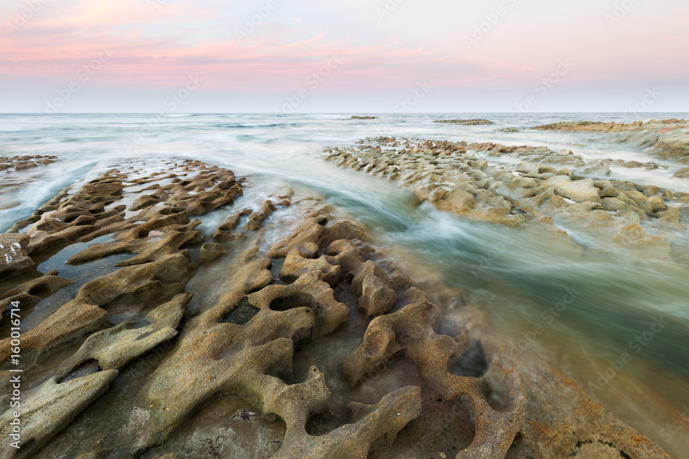 Φωτογραφία A beautiful coastal long exposure of a pink sunset over a textured limestone reef on the east coast of Australia