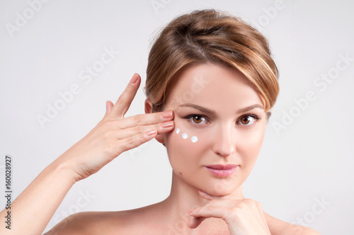 Beauty and skincare concept. Young woman applying moisturizer on face.