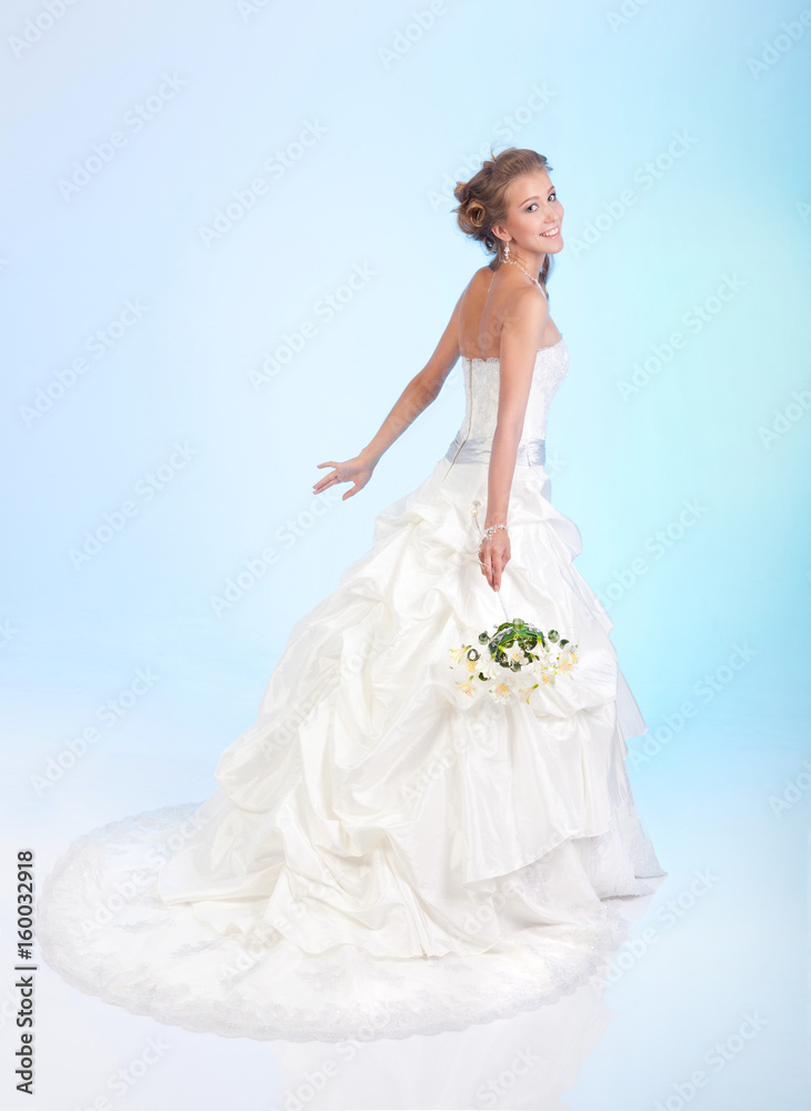 Fototapeta premium Charming bride holding a bouquet of flowers on a light blue background. Positive emotions.