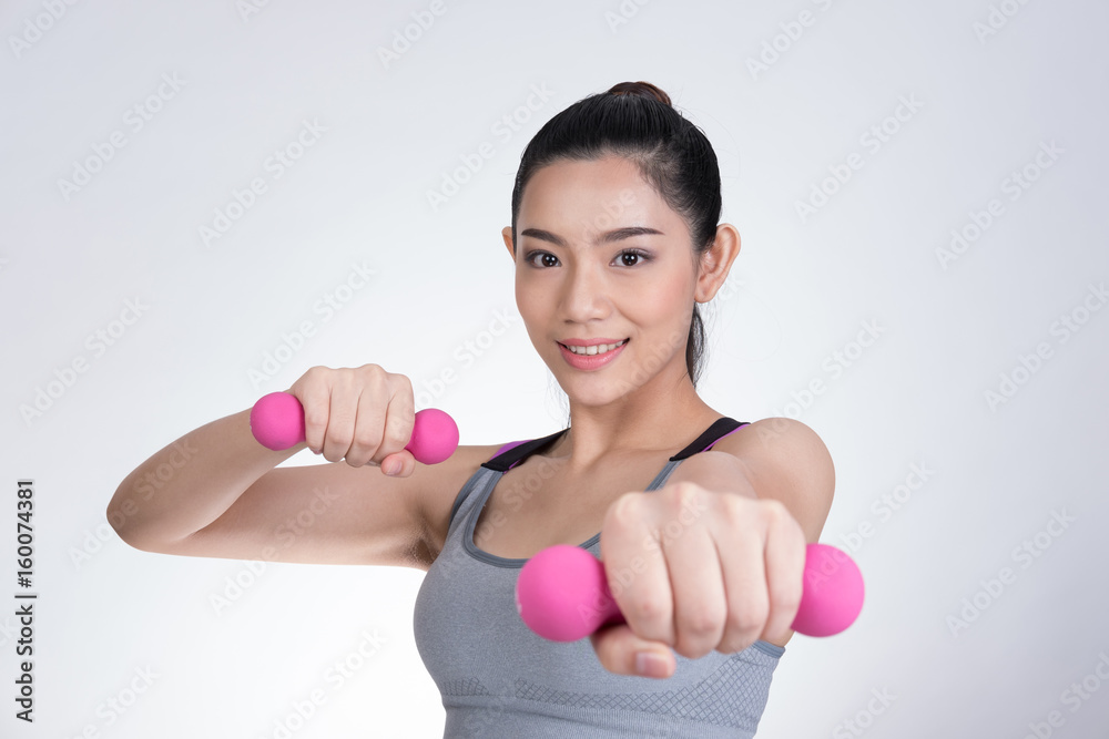 Young asian sporting woman training with dumbbell. Pretty athletic girl making physical exercise against white background. Healthy lifestyle concept. Young asian sporting woman training with dumbbell. Pretty athletic girl making physical exercise against white background. Healthy lifestyle concept.