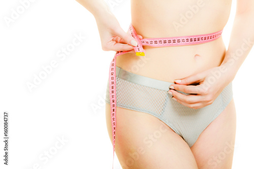 Woman in lingerie measuring her waist with measure tape.
