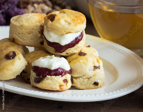 Homemade raisin scones serve with homemade strawberries jam,clotted cream and tea.Scones is English pastry for afternoon tea,cream tea.Delicious scones Devon shire or Cornish cream style. photo