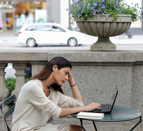 Young attractive woman sitting outside in urban park fustrated studying photo