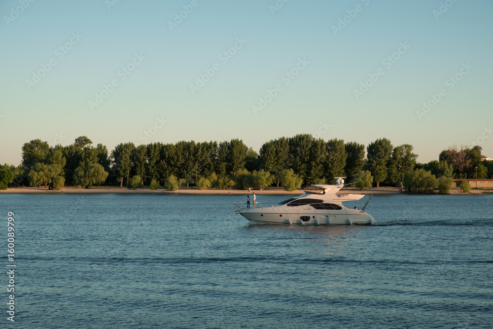 Obraz premium white boat with people sailing on the blue waters of the river on the background of green forest