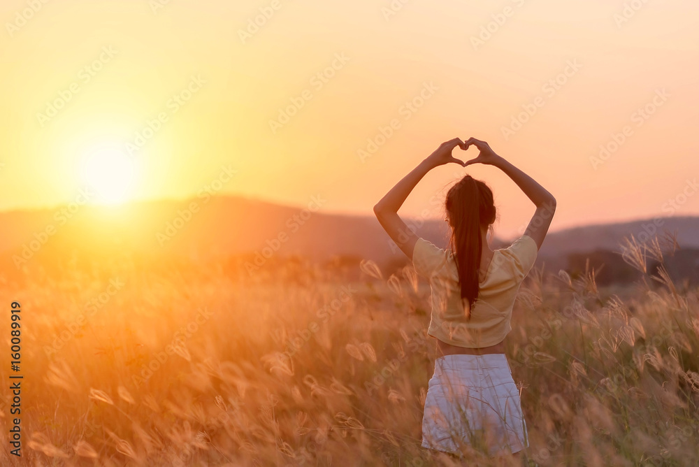 Girl making a heart-shape with her hands with mountain landscape in the background.