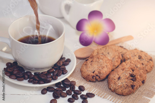 Pour coffee, cup of coffee,milk,sugar,chocolate chip cookies ,coffee beans and flower on white wooden background with loft wall style with light in concept relax time #160100121