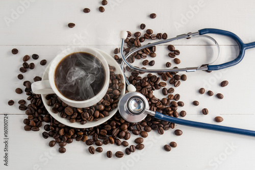 a cup of coffee ,coffee beans and stethoscope on white wooden background  in concept Health of coffee drinkers, quality of coffee