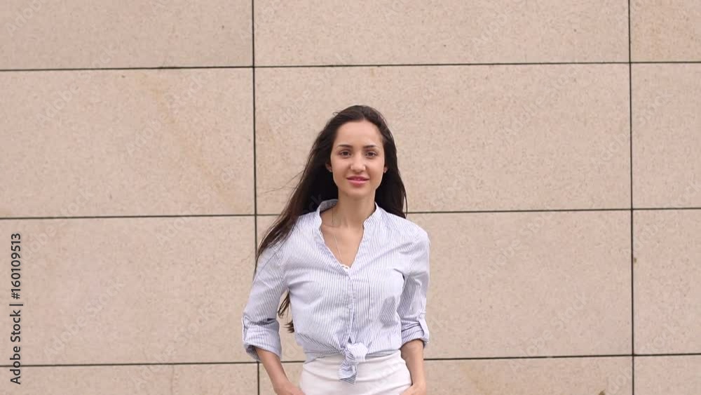 Sexy girl in white shirt and jeans walks against a white wall background and looks at the camera, close-up. Slow motion. Sexy girl in white shirt and jeans walks against a white wall background and looks at the camera, close-up. Slow motion.