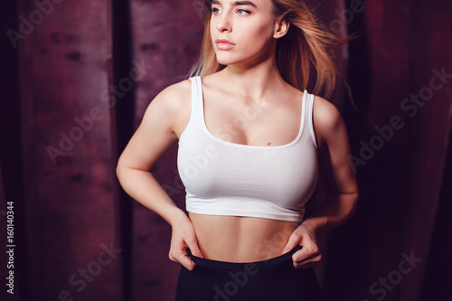Sexy blonde woman with huge breast in a white tank top standing on a dark wooden wall background. Mock-up.