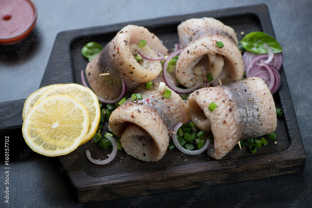 Herring rolls with spices, onion and lemon on a black wooden serving tray, horizontal shot Herring rolls with spices, onion and lemon on a black wooden serving tray, horizontal shot