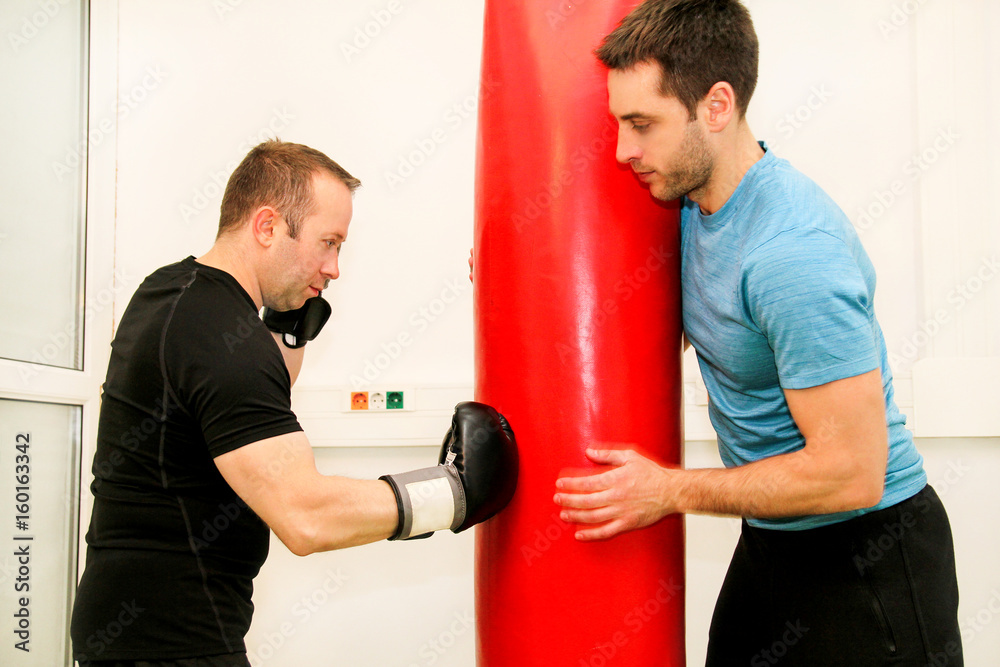 The male boxer training at gym. Athletic man punching her male partner and instructor with red boxing gloves at gym club. Attractive sports man is practicing with a handsome trainer in sport center. The male boxer training at gym. Athletic man punching her male partner and instructor with red boxing gloves at gym club. Attractive sports man is practicing with a handsome trainer in sport center.