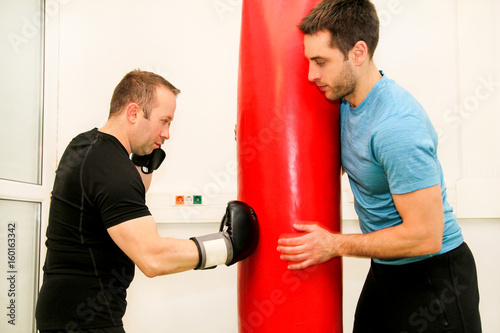 The male boxer training at gym. Athletic man punching her male partner and instructor with red boxing gloves at gym club. Attractive sports man is practicing with a handsome trainer in sport center. © zoranlino