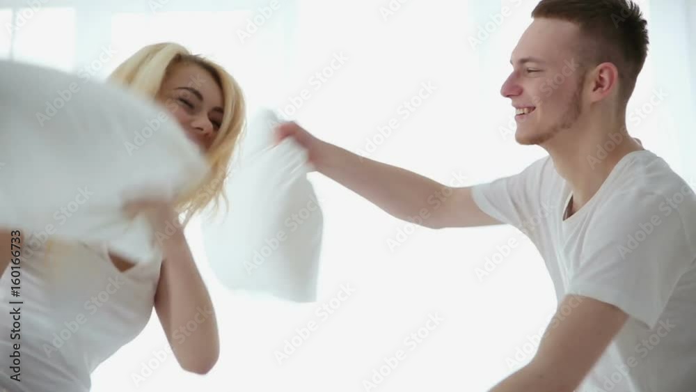 Happy young loving couple fights pillows in the bedroom Happy young loving couple fights pillows in the bedroom