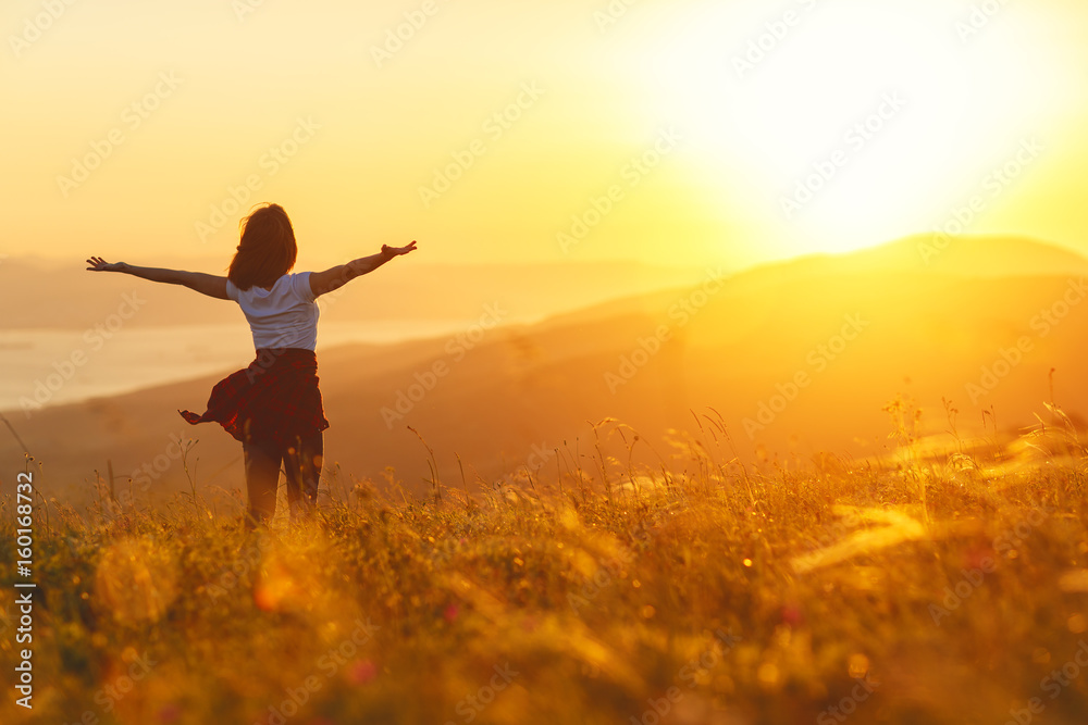 Happy woman standing with her back on sunset in nature iwith open hands.