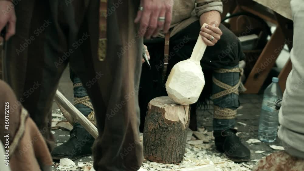 Carpenter in traditional costume hews wooden bailer with a hatchet