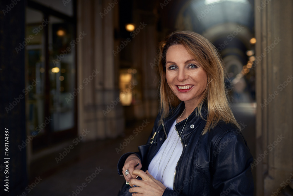 Attraktive schlanke blonde Frau steht in einer Arkade und lächelt