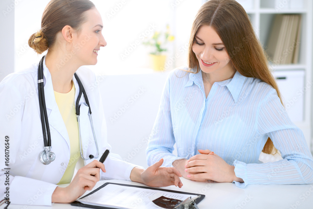 Doctor and patient have a talk while sitting at the desk near window Doctor and patient have a talk while sitting at the desk near window