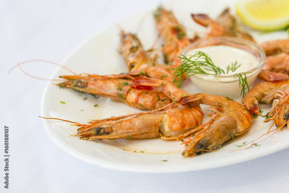 Shrimps in white plate with sauce and lemon at restaurant