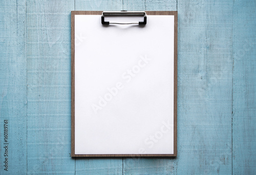 Clipboard with white sheet on wood background. Top view.Vintage style.