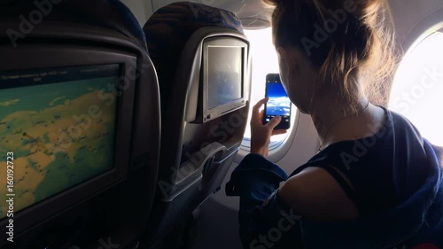 The girl climbs into the porthole and takes pictures of the landscape in the window on the phone. A young girl is traveling by plane. Slow motion 1080p