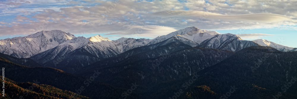 Mountain winter landscape at sunset with lenticular clouds over high snow-capped peaks. Caucasus. Russia. The Caucasian reserve. View from Mount Kazachya