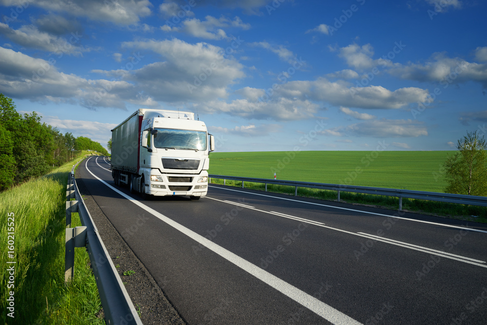 White truck driving on the asphalt road along the green fields and alleys in the countryside