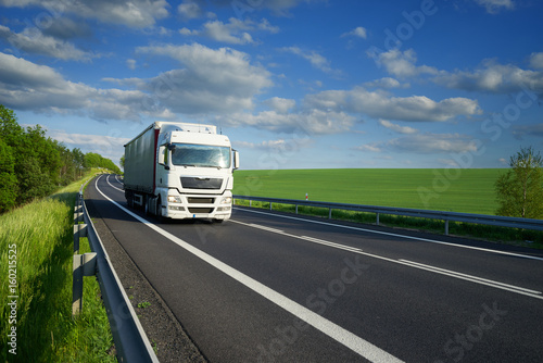 Obraz na płótnie White truck driving on the asphalt road along the green fields and alleys in the countryside w salonie
