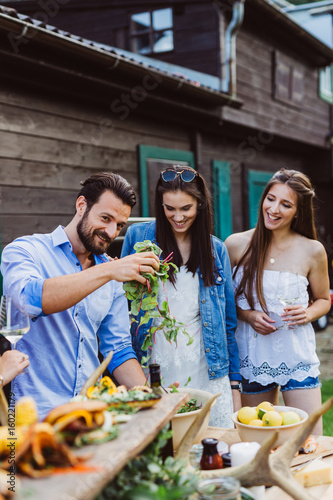 Man pouring olive oil into salad with girls at barbecue outdoors